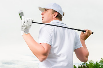 golfer in a cap against the sky with a golf club