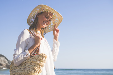 happy fashion blonde girl smiling portrait in the beach, wearing hat, a bag, shorts and white shirt, in the beach, profile photo