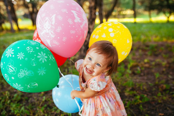 Baby girl 2-3 year old holding balloons outdoors. Birthday party