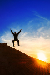 man jumping over a mountain at sunset