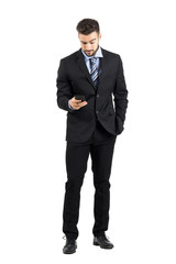 Obraz na płótnie Canvas Young business man in suit reading message on his cellphone. Full body length portrait isolated over white studio background. 