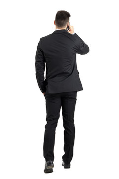 Young business man talking on the phone walking away rear view. Full body length portrait isolated over white studio background. 