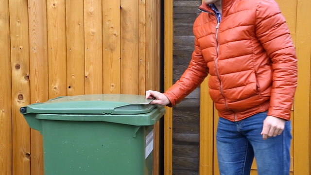 Man throwing garbage into litter-box in outside and leaving.