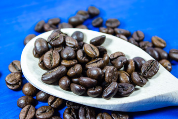 Coffee beans in wooden spoon on blue background