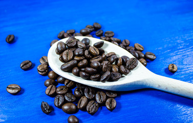 Coffee beans in wooden spoon on blue background