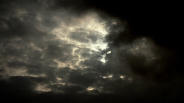 4K sun hides behind dark storm clouds time lapse with light rays