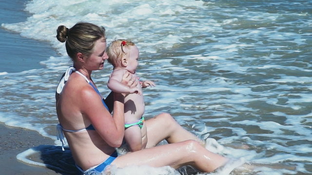 mother and her child sitting on the beach in the water slow motion 