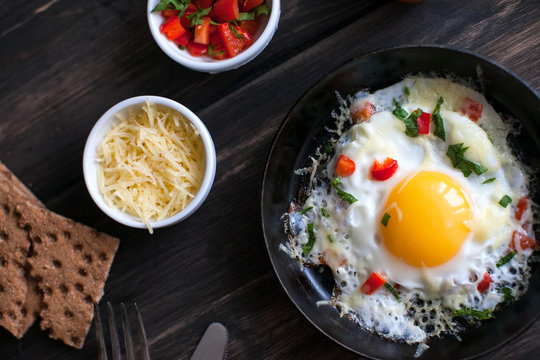 fried eggs in a frying pan with cheese, tomatoes, pepper and greens