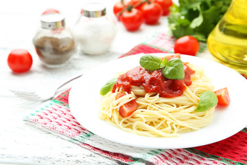 Spaghetti with tomatoes and basil on plate on white wooden backg