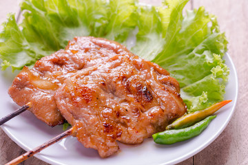 Pork grill with fresh vegetables in white plate on wooden table.