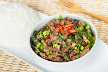 Stir fried chopped meat with chili and basil in white bowl and separated steamed rice on white plate