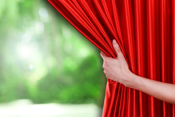 Human hand opens red curtain on nature background