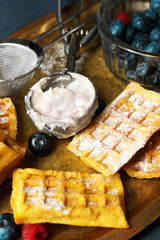 Sweet homemade waffles and blueberries on tray, on color wooden background