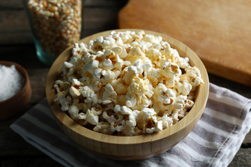Salted popcorn in a bowl on stripped napkin with board and glass of corns on wooden table