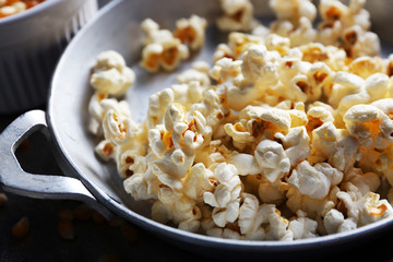 Salted popcorn in a metal bowl with cup of corns on wooden table, close up