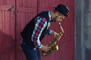 Young man playing on saxophone outside near the old wall
