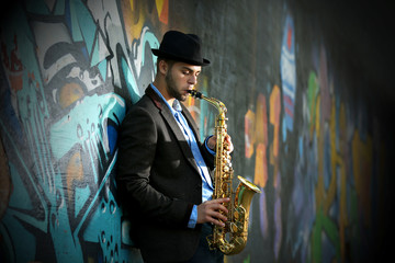 Young man with saxophone outside near the old painted wall
