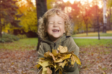 Adorable smiley kid playing with leaves in park, selective focus on face