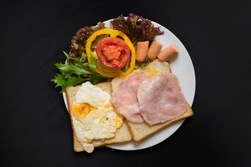 Top view of sandwiches with salad, ham, chicken sausages and tomatoes on dark background