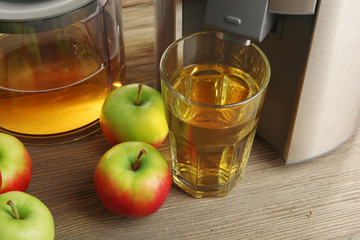 Stainless juice extractor with apples and glass of juice on wooden background, close up