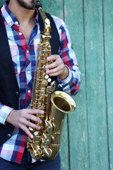 The musician plays saxophone on green wooden background, close up