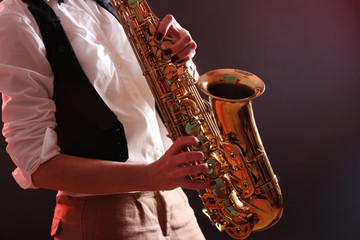 Obraz premium Saxophone in female hands on dark background, close up