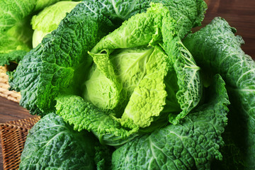 Savoy cabbage in wicker basket on wooden background, close up