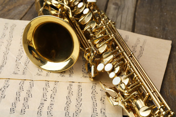 Obraz premium Beautiful golden saxophone with musical notes on wooden background, close up