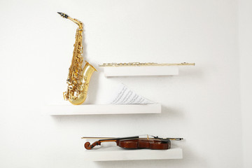 Violin, flute and saxophone on decorated shelves against white wall background