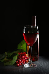 A bottle and a glass of wine, red grapes, on grey-black background