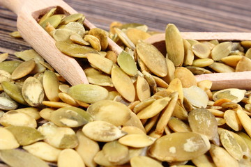 Pumpkin seeds with spoon on wooden background