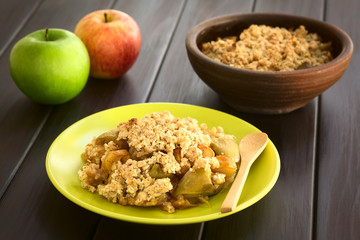 Freshly baked apple crumble or crisp served on plate with wooden spoon, photographed on dark wood with natural light (Selective Focus, Focus one third into the crumble)