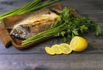 On a wooden table plate with two roasted carp fish dorado