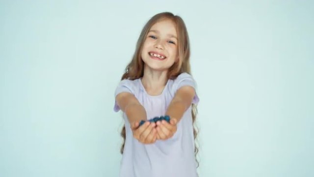 Girl holding in handful blueberry sniffing and showing at camera on the white background. Happy child with fruits