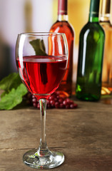 Red wine glass with colourful bottles on wooden table against unfocused background