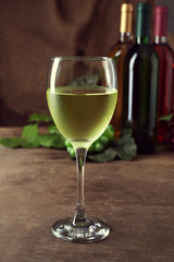 White wine glass against different bottles and grape on wooden table