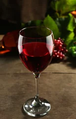 Fotobehang Rode wijnglas tegen rieten mand met druif en wijnfles op houten tafel © Africa Studio
