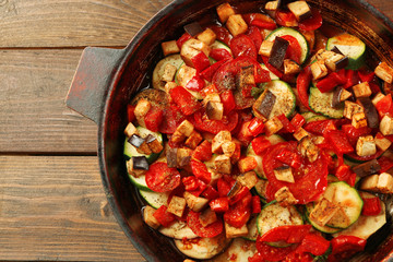 Tasty vegetarian ratatouille made of eggplants, squash, tomatoes and onions in black cast iron pan, on wooden table background