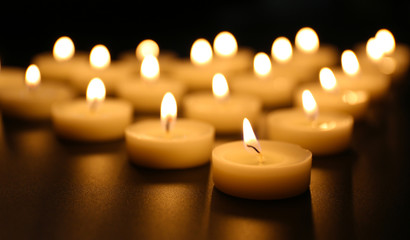 Alight candles in a row on black background, blurred