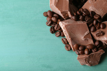 Milk chocolate pieces and coffee grains on color wooden background