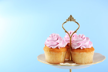 Tasty cupcakes on stand, on color background