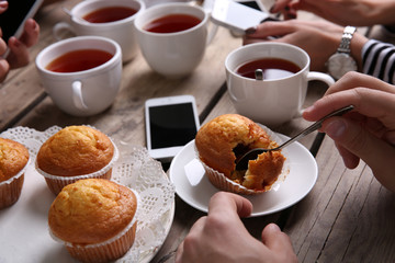 Four hands with smart phones holding  cups with tea, on wooden table background