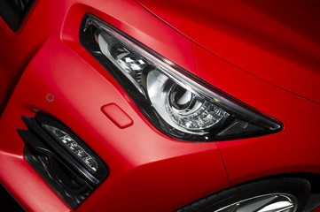 Predatory car headlight and hood of powerful sports car with matte red paint and wheel with silver disc 