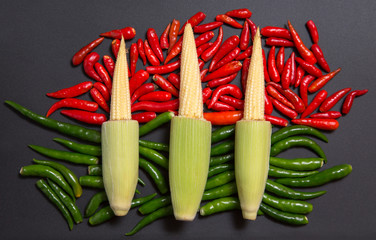 Fresh raw baby corn cobs on red and green non-stem chili peppers