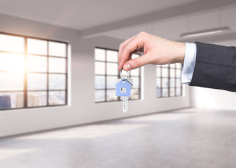 A man in formal suit holds a key in a modern loft panoramic apartment or office. Rent or buy new...