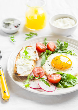 fried egg, fresh vegetable salad and a grilled cheese sandwich on a light plate on white background - healthy Breakfast