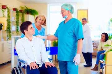 Fototapeta premium surgeon and medical staff talking with young adult man in wheelchair, in hospital