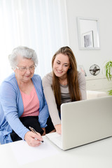 cheerful young woman teaching computer to an old senior woman at home