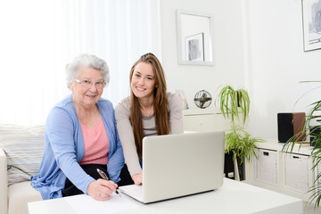 cheerful young woman teaching computer to an old senior woman at home