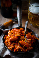 stewed cabbage with sausages in a vintage frying pan and a mug with beer.